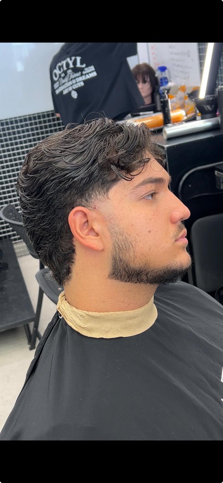 Perfil lateral de un cliente sentado con el pelo texturizado y la barba perfilada.